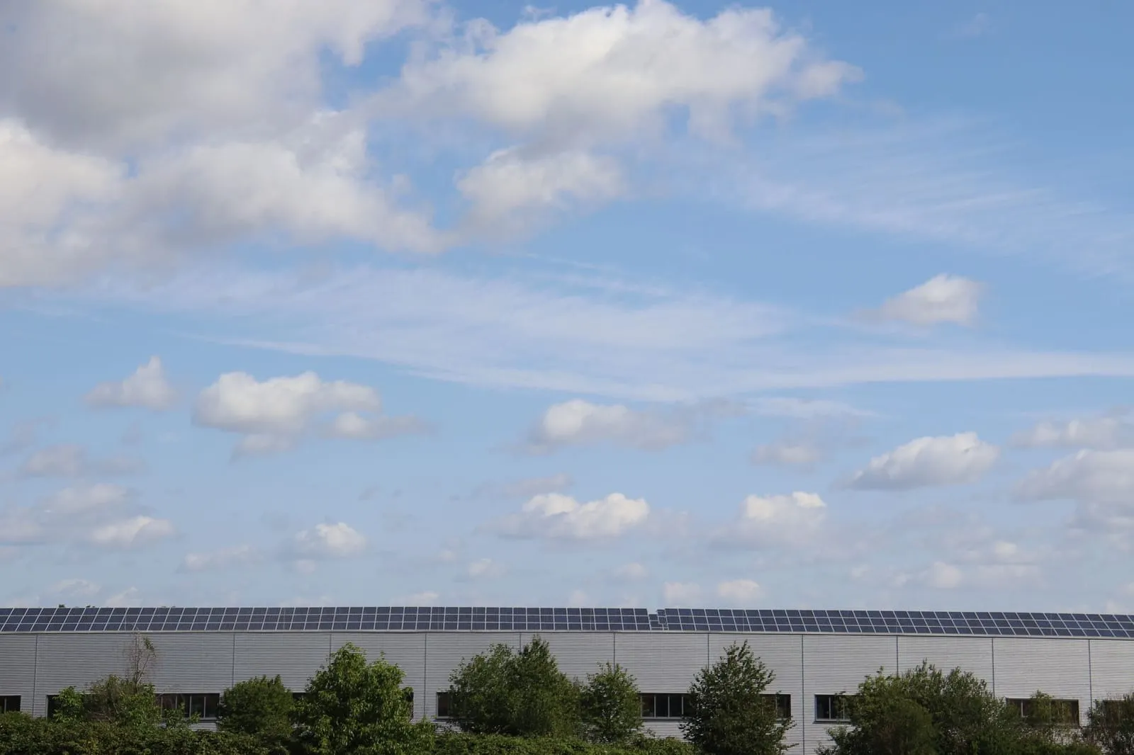 A large industrial commercial building with a rooftop solar array laid in tilted rows across its flat roof, illustrating a re-roof engineered to carry a future ballasted PV load